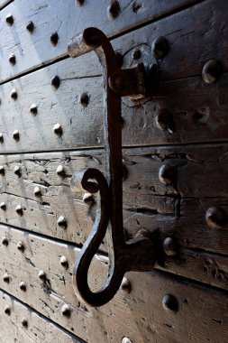 Eski metal düğümün ayrıntıları ahşap kapının gölgesinde, eski kapının dokusu metal perçinlerle aydınlanıyor güneş ışığıyla 