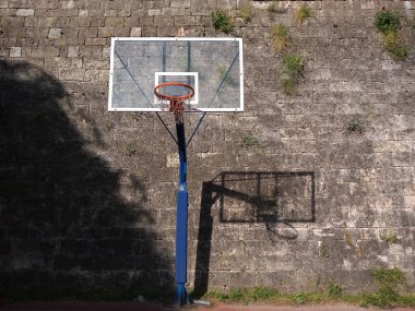 Kayalık duvarda gölgesi olan sepet tahtası, güneşli sabahın erken saatlerinde açık hava spor aktivitesi.
