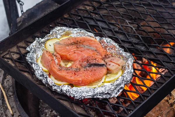 I pezzi di salmone su fette di limone su lamina di metallo sono grigliati sopra un fuoco. — Foto Stock