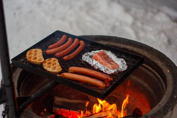 Salmón, salchichas y pan en la parrilla sobre el fuego. — Foto de Stock