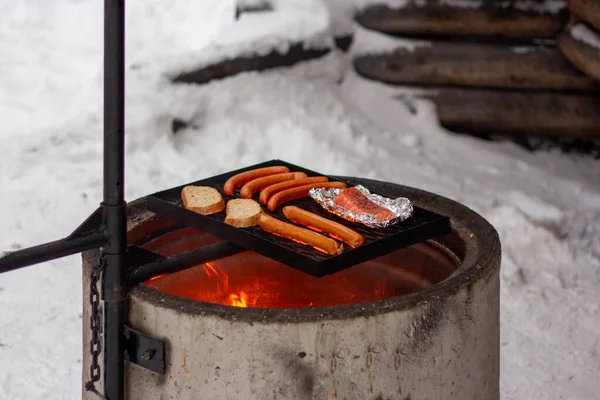 Salmón, salchichas y pan en la parrilla sobre el fuego. — Foto de Stock