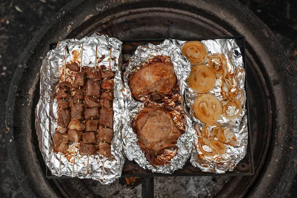 Pork kebab, pork steaks and onions are grilled on the foil over a campfire. — Stock Photo, Image