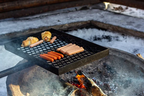 Embutidos y bollos de salchicha en una parrilla de barbacoa sobre un fuego. — Foto de Stock