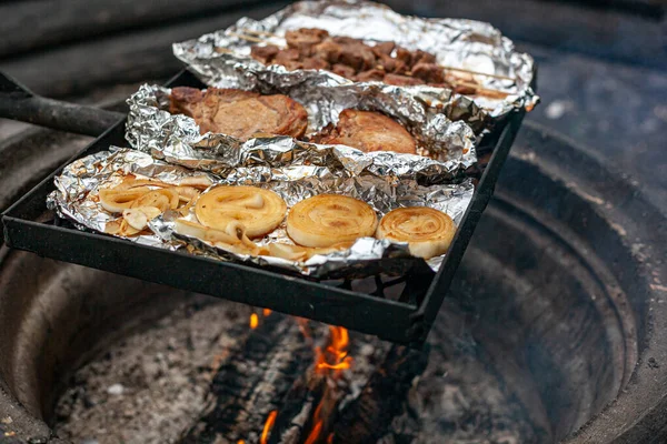 Fläskkebab, fläskstek och lök grillas på folien över en lägereld. — Stockfoto