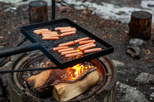 The sausages are grilled on the black iron grid over a campfire. — Stock Photo, Image