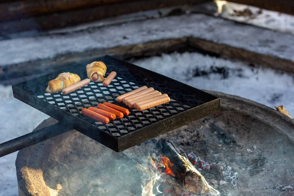 Kolbász és kolbászos zsemle grillsütőn a tűz felett. — Stock Fotó