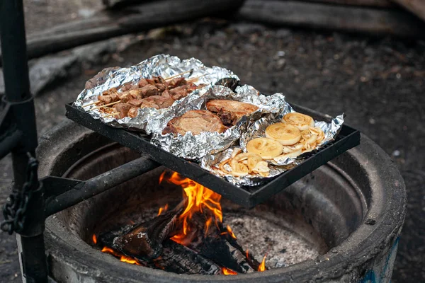 Kebab de cerdo, filetes de cerdo y cebollas se asan a la parrilla en el papel de aluminio sobre una fogata. — Foto de Stock