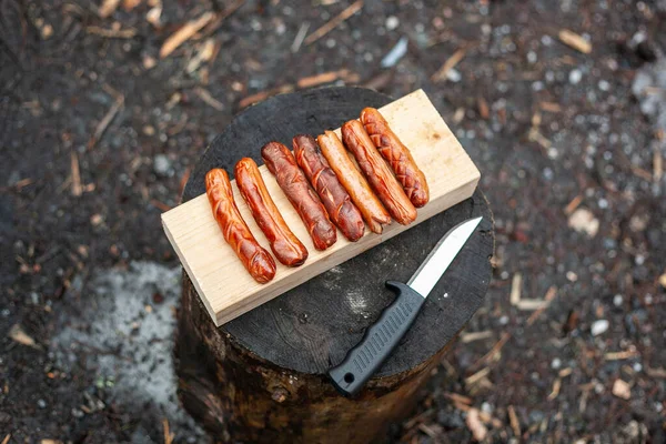 На грилі лежать ковбаски на дерев'яній дошці і ніж на пні . — стокове фото