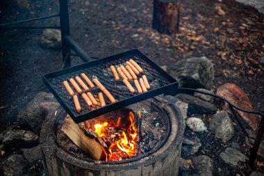 Sosisler bir kamp ateşinin üzerinde ızgarada kızartılıyor..
