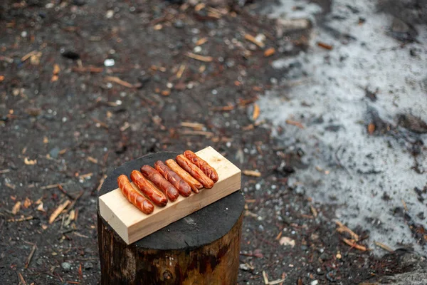 Сосиски на гриле лежат на деревянной доске на пне. — стоковое фото
