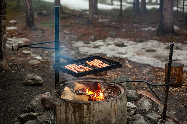 A kolbászt a fekete vasrácson grillezik egy tábortűz felett.. — Stock Fotó