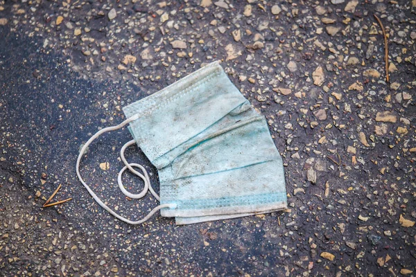 Schmutzige medizinische Gesichtsmaske auf dem Fußboden auf der Straße. Gebrauchte Chirurgenmasken planlos auf dem Bürgersteig verstreut, selektiver Fokus — Stockfoto