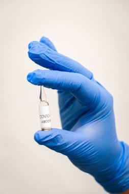 Üzerinde Covid-19 aşısı olan küçük ampule sahip mavi tıbbi eldivenleri teslim edin. Coronavirus covid 19 tedavi konsepti. 