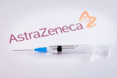 Riga, Letonya: 12 Ocak 2021: AstraZeneca Covid-19 aşı konsepti. Şırınganın yakın çekimi ve arka planda AstraZeneca şirketinin logosu. Odaklanmamış