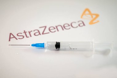 Riga, Letonya: 12 Ocak 2021: AstraZeneca Covid-19 aşı konsepti. Şırınganın yakın çekimi ve arka planda AstraZeneca şirketinin logosu. Odaklanmamış