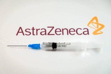 Riga, Letonya: 12 Ocak 2021: AstraZeneca Covid-19 aşı konsepti. Şırınganın yakın çekimi ve arka planda AstraZeneca şirketinin logosu. Odaklanmamış