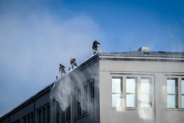 Riga, Letonya: 12 Şubat 2021: Erkek işçiler emniyet kemerlerinde küreklerle kardan binaların çatısını temizledi. Seçici odak