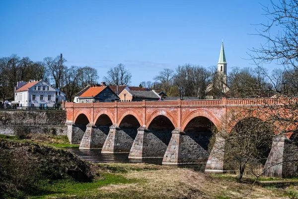 Kuldiga, Letland - 1 mei 2021: Landschap met rivier, historische bakstenen brug en Venta rivier in stad Kuldiga, Letland — Stockfoto