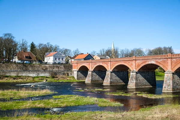 Kuldiga, Łotwa - 1 maja 2021: Krajobraz z rzeką, zabytkowy most murowany i rzeka Venta w mieście Kuldiga, Łotwa — Zdjęcie stockowe