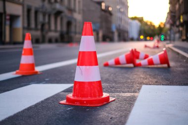 Bright orange traffic cones standing in a row on dark asphalt in the city. Road works. Selective focus
