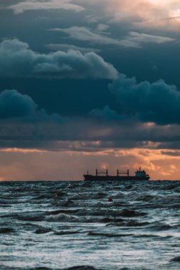 Denizde güneş batıyor, kargo gemisi manzaralı. Bulutlar ve fırtınalı deniz. Odaklanmamış.