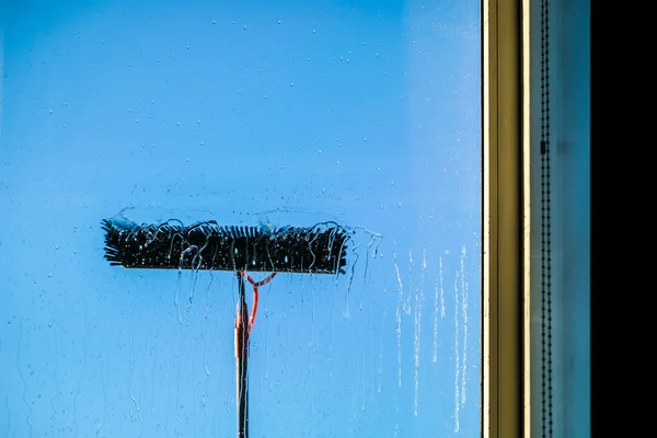 Window cleaning using telescopic water brush and wash system. Commercial window cleaning from the outside with sky in background. Defocused