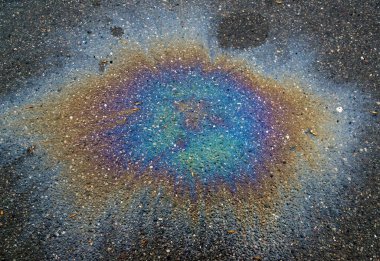 Islak asfaltta renkli gaz lekesi. Bu, bir arabanın ya da kamyonun altındaki sızıntıdan kaynaklanan bir leke..