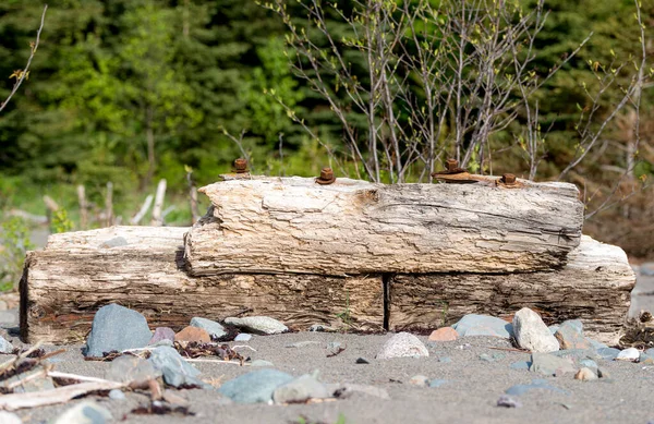 An old, broken piece of a pier or wharf lying on a beach. The wood is worn and the bolts holding the pieces together are rusty. There is room for text.