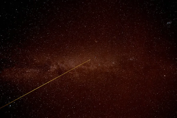 A laser beam shoots into the night sky. Part of the Milky Way visible. Many stars. The laser beam is yellow.