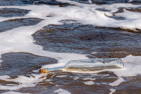 A message in a bottle floating in the ocean. Foam and seaweed bits around bottle, cork in end. Bright sunny day.