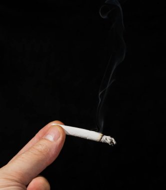 Siyah bir arka plan önünde marihuana sigarası tutan bir el. Esrar yakılıyor ve ondan duman yükseliyor. Tepede mesaj için yer var..