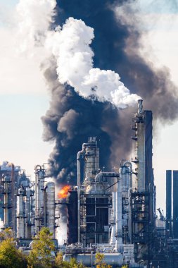 Patlamadan sonra petrol rafinerisinde yangın ve siyah duman çıktı. Duman ve alevin önünde görünen kuleler. Sahne uçucu havadan dolayı biraz bulanık..