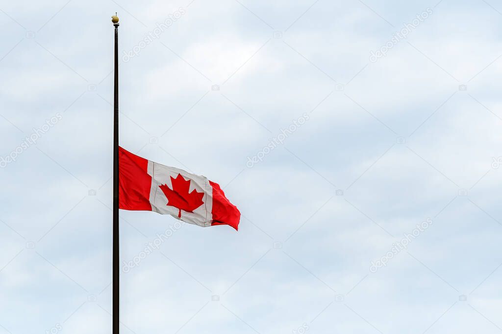 A Canadian flag at half mast, lowered in remembrance of the indigenous children who were abused and dies in residential schools. Overcast, wide view.