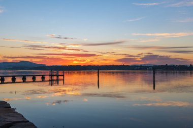 Gündoğumu, yüksek bulutlu ve yansımalı su manzarası Orta Sahildeki Woy Woy rıhtımında, NSW, Avustralya.