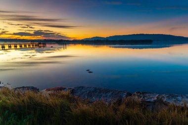 Gündoğumu, yüksek bulutlu ve yansımalı su manzarası Orta Sahildeki Woy Woy rıhtımında, NSW, Avustralya.