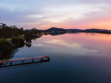 Orta Sahildeki Woy Woy rıhtımında bulutlu ve yansımalı güzel ve yumuşak gün doğumu, NSW, Avustralya.