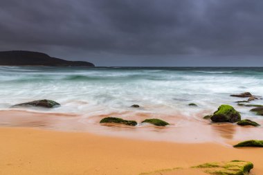 Central Coast, NSW, Avustralya 'daki Killcare Sahili' nde canlı yeşil yosunlu kayalarla bulutlu bir deniz doğumu..