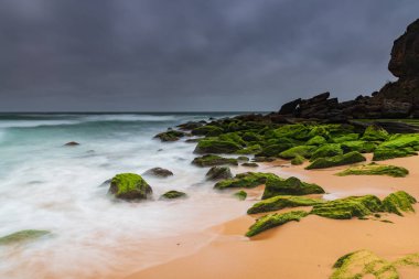 Central Coast, NSW, Avustralya 'daki Killcare Sahili' nde canlı yeşil yosunlu kayalarla bulutlu bir deniz doğumu..
