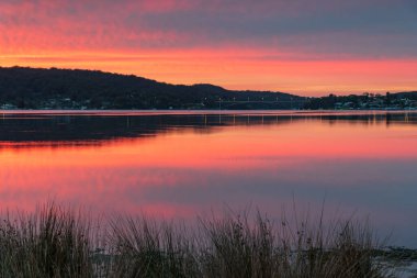 Gündoğumu ve yansımaları, Avustralya, NSW 'deki Woy Woy rıhtımında yüksek bulutlu bir su manzarası..