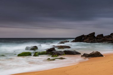 Bulutlar bulutlu gündoğumu deniz manzarası ile kaplıydı. Central Coast, NSW, Avustralya 'daki Killcare Plajı' nda kayalar vardı..