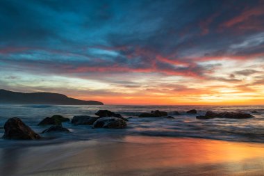 Deniz üzerindeki yüksek bulutlar, Orta Sahildeki Killcare Sahili 'nden mavi, pembe ve turuncu gündoğumu, NSW, Avustralya.