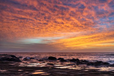 Central Coast, NSW, Avustralya 'daki North Avoca Sahili' nde yüksek bulutlu ve tesselleştirilmiş kaya platformu ile renkli gündoğumu deniz manzarası.