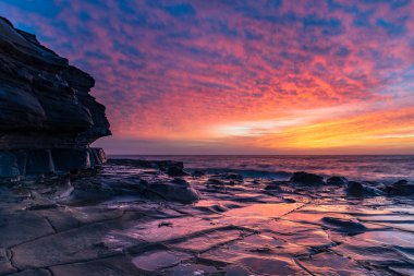 Central Coast, NSW, Avustralya 'daki North Avoca Sahili' nde yüksek bulutlu ve tesselleştirilmiş kaya platformu ile renkli gündoğumu deniz manzarası.