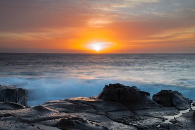 Central Coast, NSW, Avustralya 'daki North Avoca Sahili' nde yüksek bulutlu ve tesselleştirilmiş kaya platformu ile renkli gündoğumu deniz manzarası.