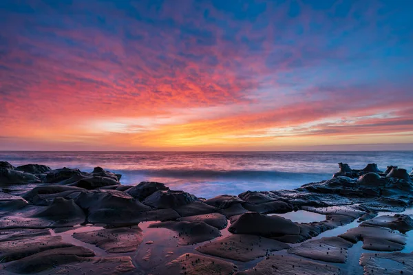 Central Coast, NSW, Avustralya 'daki North Avoca Sahili' nde yüksek bulutlu ve tesselleştirilmiş kaya platformu ile renkli gündoğumu deniz manzarası.