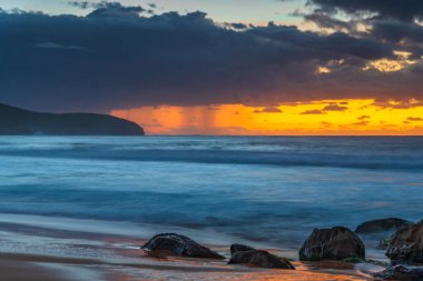 Sabahın erken saatlerinde kumsalda gökyüzünde dalgalar ve yağmur bulutlarıyla Killcare Sahili, NSW, Avustralya.