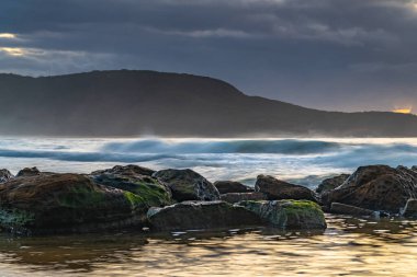 Sabahın erken saatlerinde kumsalda gökyüzünde dalgalar ve yağmur bulutlarıyla Killcare Sahili, NSW, Avustralya.
