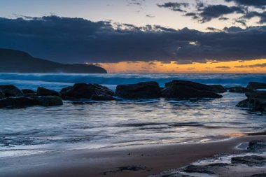 Sabahın erken saatlerinde kumsalda gökyüzünde dalgalar ve yağmur bulutlarıyla Killcare Sahili, NSW, Avustralya.