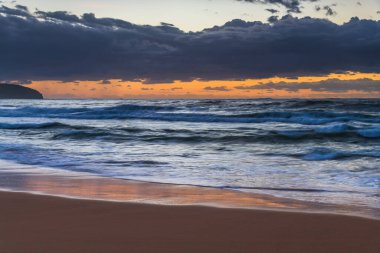Sabahın erken saatlerinde kumsalda gökyüzünde dalgalar ve yağmur bulutlarıyla Killcare Sahili, NSW, Avustralya.