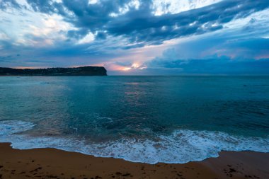 Gündoğumu deniz manzarası sörfçülerle, deniz havuzu, burunlar, bulutlar ve MacMasters Sahili 'nden denize doğru bir fırtına Central Coast, NSW, Avustralya.